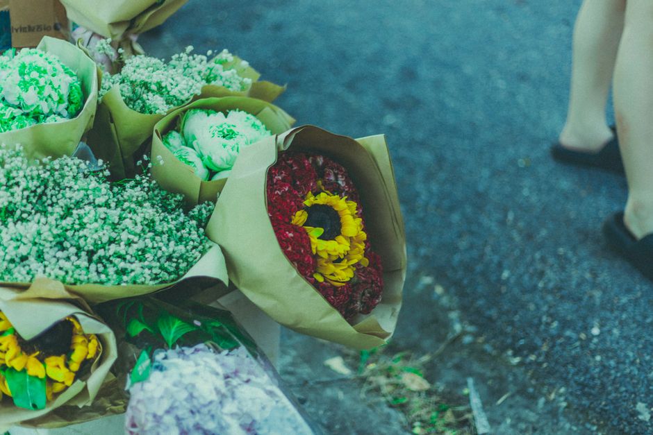 A collection of freshly arranged flower bouquets wrapped in light brown paper, featuring a variety of vibrant blooms including red and yellow chrysanthemums, white baby's breath, and green foliage. Th